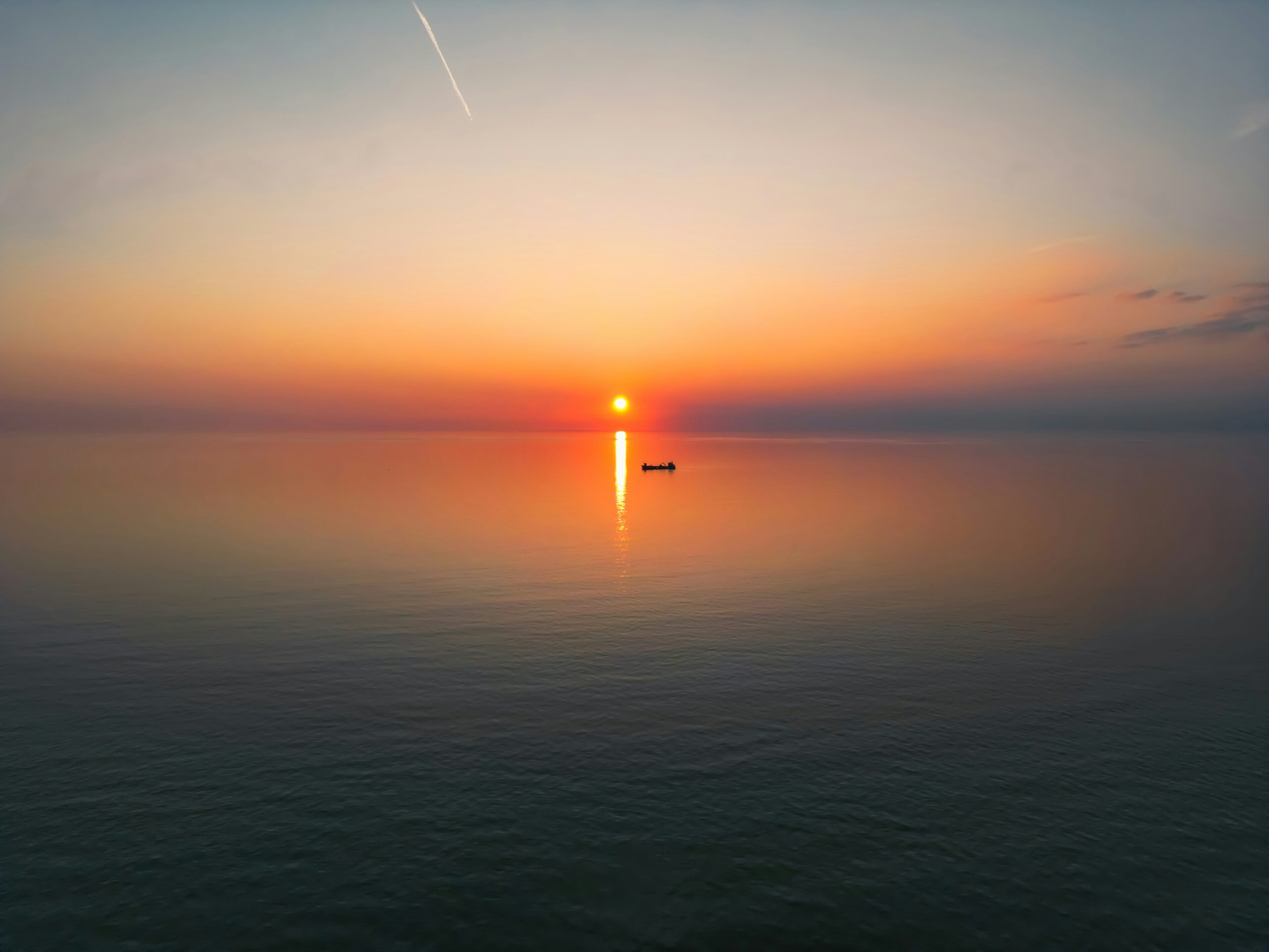The sun is setting over the water with a boat in the distance